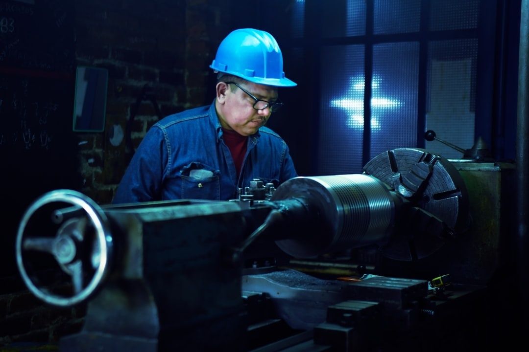 Worker in a blue hard hat operating a precision metalworking lathe